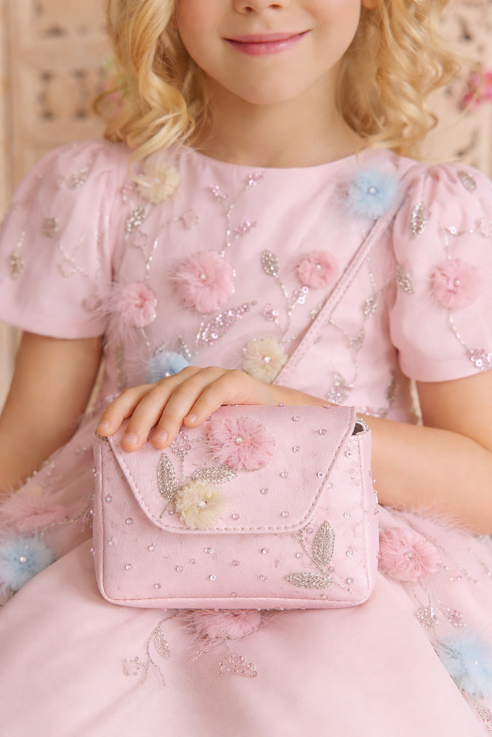Child in a pink dress holding a matching pink handbag with floral designs.