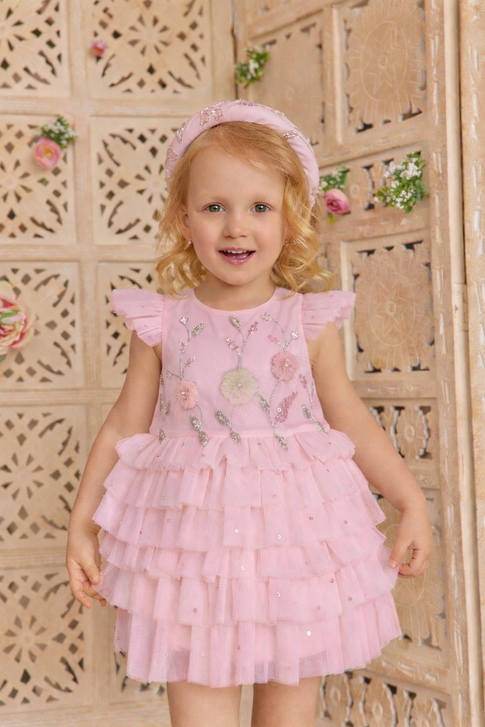 Young girl wearing a pink dress with floral embroidery.
