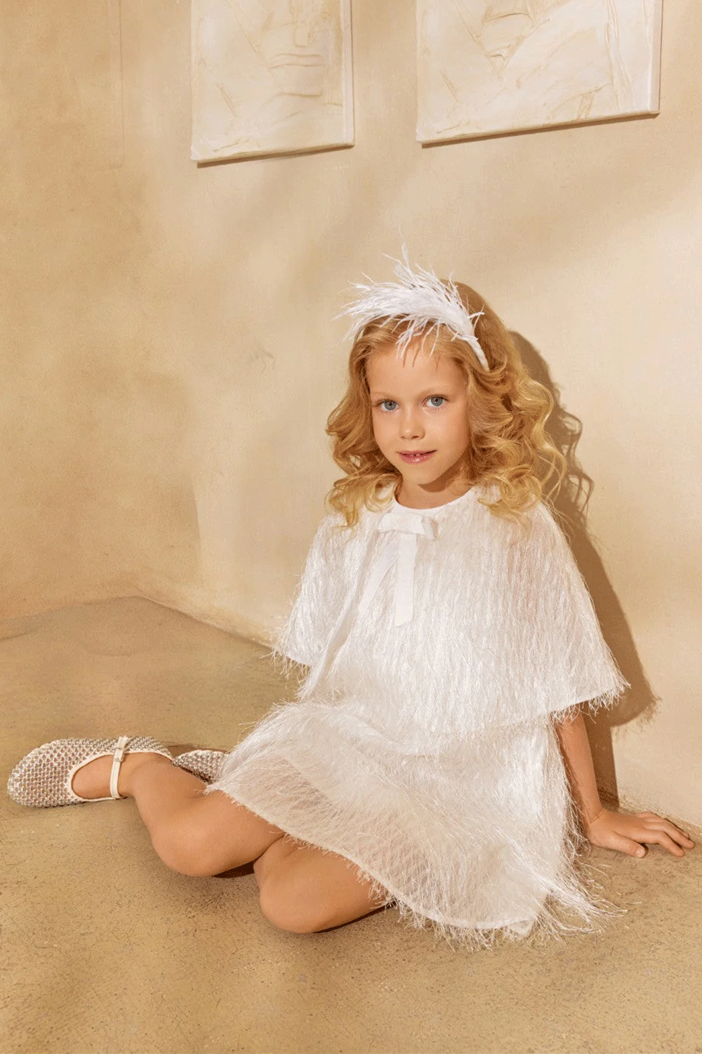 White dress with textured fringe shimmering fabric, featuring a cape-effect overlay and a bow detail
